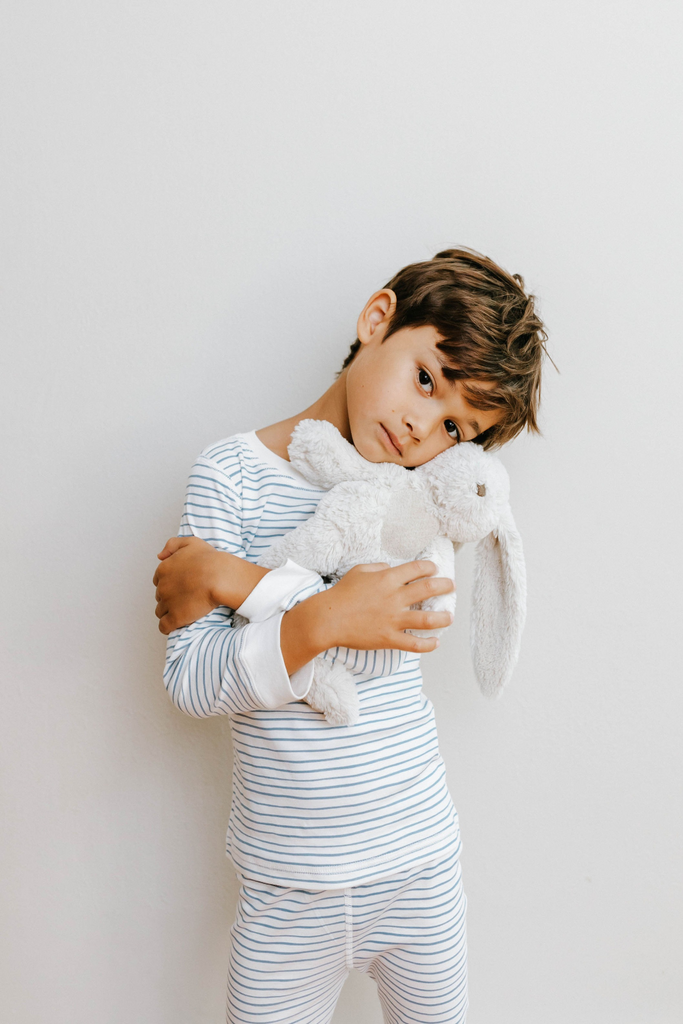 boy holding a stuffy and wearing a blue striped organic pima cotton pajamas